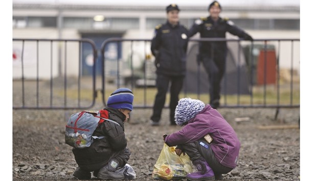 Migrant children search through a bag while being observed by police officers, at a refugee transit camp in Slavonski Brod, Croatia.