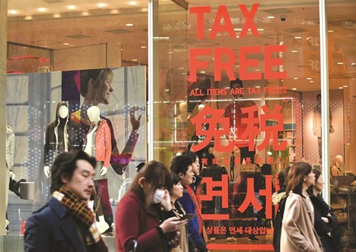 Pedestrians walking on a street past a clothes shop displaying characters of u2018Tax Freeu2019 in Tokyo. Japanu2019s bid to revive its once-soaring economy is on the ropes as an equity market bloodbath and resurgent yen threaten to knock Prime Minister Shinzo Abeu2019s growth plan to the canvas.