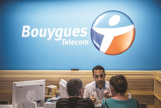 An employee speaks with customers as they sit inside a Bouygues Telecom store in Paris. Journal du Dimanche said Free is looking at buying Bouyguesu2019 network and frequencies for about u20ac2bn.