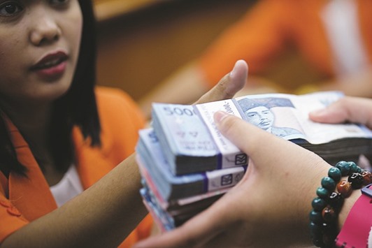 A customer hands over bundles of Indonesian 50,000 rupiah notes to a customer at a currency exchange office in Jakarta. The rupiah is the top-returning emerging-market currency in the past six months.