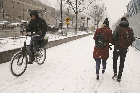 A cyclist passes pedestrians on a sidewalk on 12th Avenue in the Manhattan borough of New York City as snow falls on Monday.