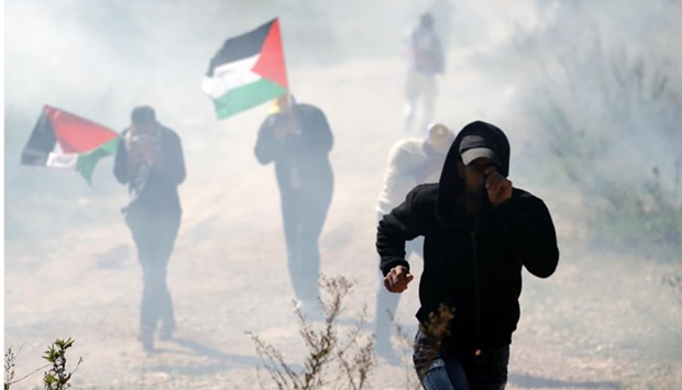 Palestinian protesters, some holding national flags, run away from tear gas smoke during clashes with Israeli security forces following a march on February 19, 2016 in the West Bank village of Bilin, near Ramallah. AFP