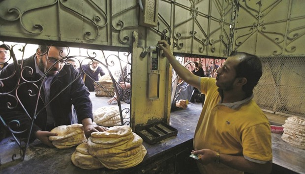 People queue for subsidised bread as a bakery worker looks at a smart card reader in the Suez Canal city of Port Said, 170km (106 miles) northeast of Cairo (file). The most populous Arab nation has seen wheat prices jump, prompting Egypt to scrap three tenders in two weeks.
