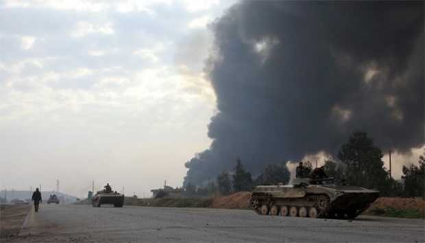 Syrian government forces drive tanks near smoke billowing in Aleppo