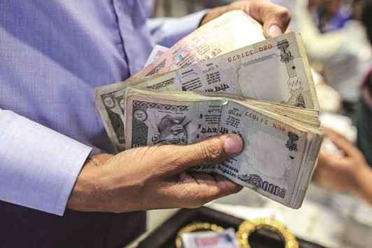 A salesperson holds Indian rupee banknotes at a jewellery store in Mumbai. The currency fell 0.2% to 68.60 a dollar yesterday.