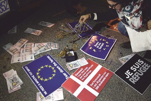 A woman leaves some jewellery in front of police officers standing guard in front of the Danish embassy in Athens during a protest yesterday against Denmarku2019s anti-migrant laws. The Danish parliament has passed a package of measures to deter refugees from seeking asylum, including confiscating valuables to pay for their stay, despite protests from international human rights organisations.