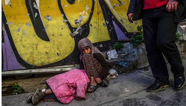 A man walks past a Syrian girl who begs in the street as another child sleeps next to her, in downtown Istanbul. AFP
