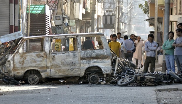 People stand behind damaged motorcycles and a van that were set alight by protesters in Haryana