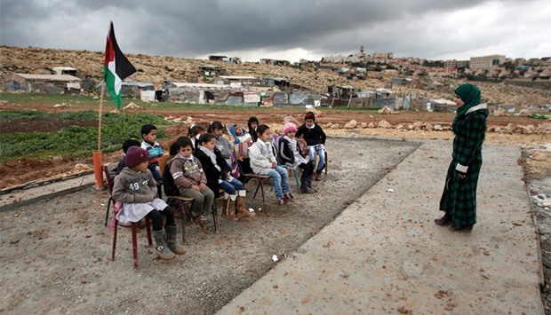 A Palestinian teacher leads a class of Palestinian bedouin children from the Abu Anwar community near the Jewish settlement of Maale Adumim (background), in the West Bank city of al-Azariya, east of Jerusalem, yesterday. Israeli Army forces dismantled prefab classrooms and homes built with a donation from the French government, on February 20, and forced the children to attend their class outside without any infrastructure and under bad weather conditions.