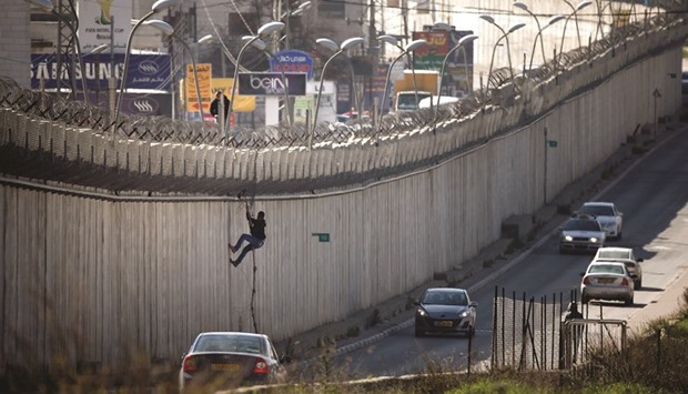 A Palestinian man uses a rope to climb over a section of Israelu2019s controversial barrier that separates the West Bank city of Al-Ram from east Jerusalem yesterday. Many Palestinians from the West Bank cross illegally into Israel daily in search for work.