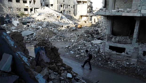 Syrian man walks along a street damaged by shelling