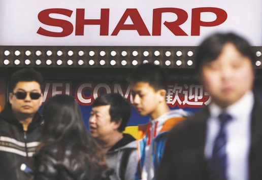 A logo of Sharp is seen above Chinese tourists standing outside an electronics retail store in Tokyo. The Japanese firm said yesterday that it has been disclosing contingent liabilities properly in its financial statements u2013 comments which come after Foxconn put its takeover of the ailing electronics maker on hold, citing new material information.