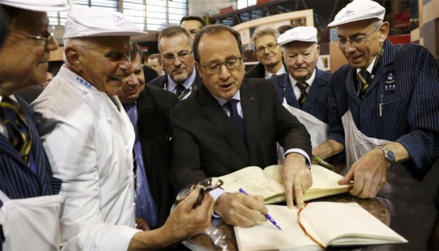 French President Francois Hollande (C) signs a guest book during his visit to the International Agri