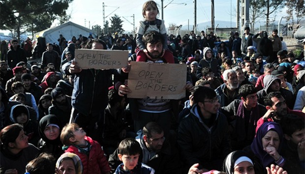 Men hold banners as migrants demonstrate as they wait to cross the Greece Macedonian border