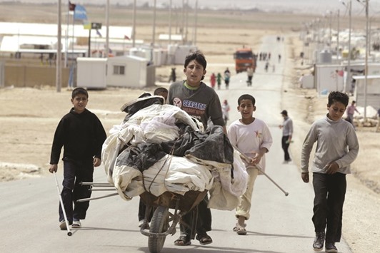 This file photo taken on April 15, 2014 shows Syrian  boys pushing a wheelbarrow along a road in Zaatari refugee camp, north east of the Jordanian capital Amman. On the doorstep of Syriau2019s conflict, Jordan is pinning hopes on the donor conference in London tomorrow  to ease the burden on its debt-riddled economy of hosting hundreds of thousands of refugees.