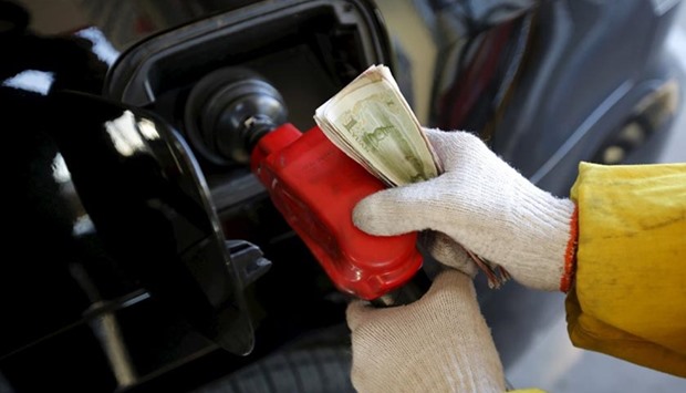A gas station attendant holds money as he feeds fuel into a customer's car at a filling station in Beijing.