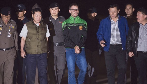 Spanish national Artur Segarra (centre), 36, walks handcuffed surrounded by police officers after he arrived by helicopter at the Tha Raeng police aviation base in Bangkok yesterday.