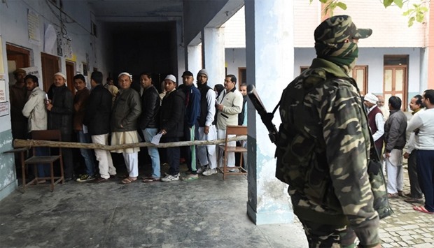 Indian security personnel stands guard as voters queue to cast their vote