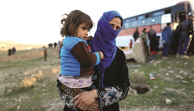 A woman, who just fled a village controlled by Islamic State militants, holds her daughter as she stands in front of a bus before heading to the camp at Hammam Ali, south of Mosul, Iraq yesterday.