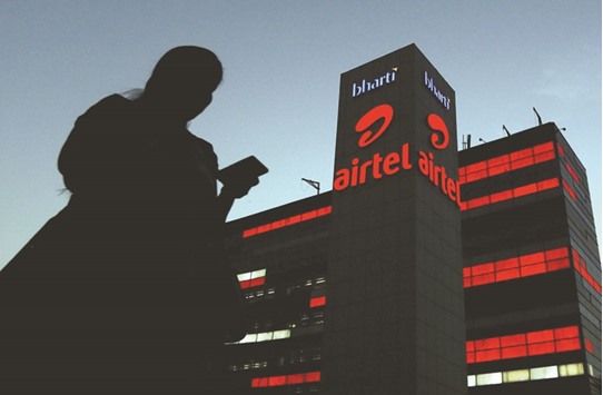 A girl checks her mobile phone as she walks past the Bharti Airtel office building in Gurugram, previously known as Gurgaon, on the outskirts of New Delhi yesterday. The companyu2019s shares surged more than 5% in Mumbai morning trade following the announcement of its deal with Telenor.