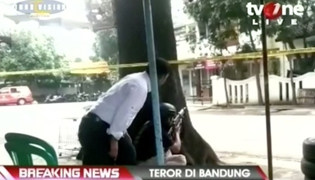 A video grab shows a policeman crouching behind a tree, outside a government building after an explosion in Bandung city