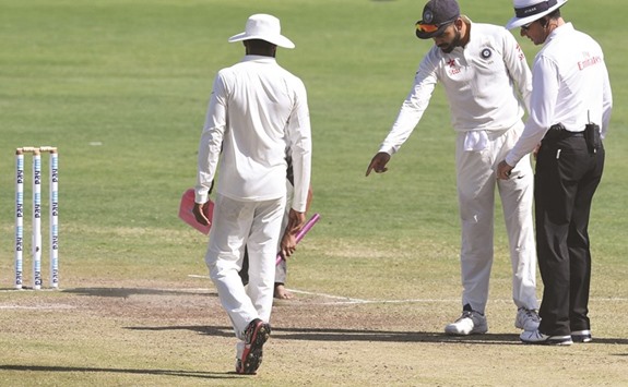 Indiau2019s captain Virat Kohli (centre) points out marks on the pitch to umpire Richard Kettleborough of England on the third day of the first Test against Australia in Pune last week. (AFP)