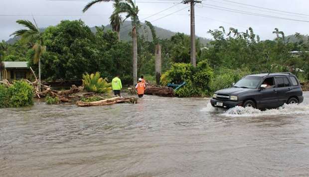 A car passing through a flooded street as Red Cross workers check on a house in the Apia area in  Samoa Island, near Tonga, after Cyclone Gita wreaked havoc on the island.