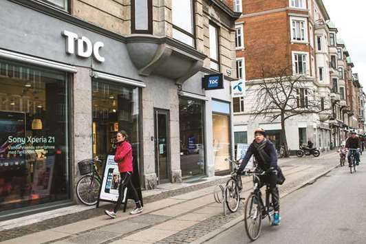 Cyclists and a jogger pass a TDC telecommunications store in Copenhagen. In total about 1,800 of MTGu2019s 3,800 employees will transfer to TDC, essentially ending 30 years of TV broadcasting for the Swedish company.