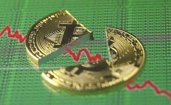 Broken representation of the Bitcoin, placed on a monitor that displays stock graph and binary codes, is seen in this illustration.