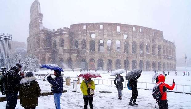 Tourists take pictures of the ancient Colosseum during a snowfall in Rome