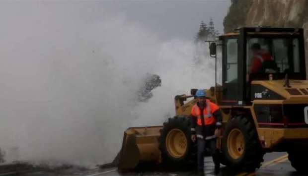 A wave hits heavy machinery as emergency personnel work on a flooded road in Nelson, NZ
