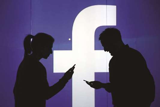 People seen as silhouettes as they check mobile devices while standing against an illuminated wall bearing Facebooku2019s logo in this arranged photograph in London. Facebook, which has more than 2bn people logging in monthly, has never failed to grow its user base.