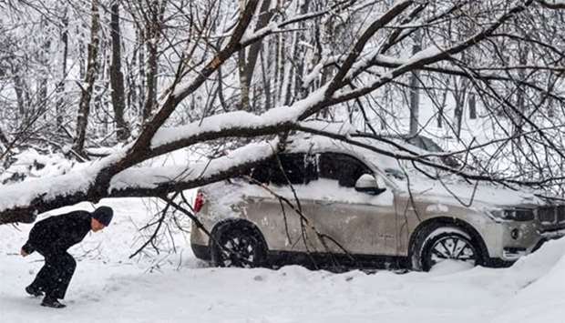 A man walks under a tree lying on a car after a snowstorm in Moscow on Monday.