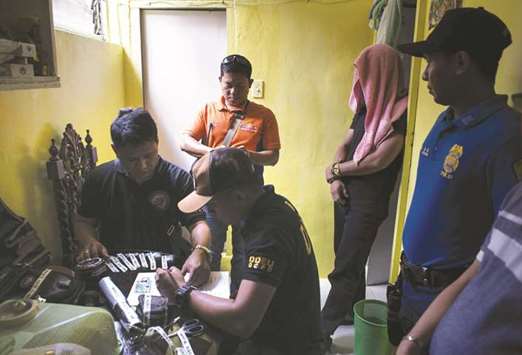 Police investigate drug paraphernalia discovered as a suspect (second right) covers his face after a drug raid in Manila yesterday.