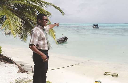 In this file photo, local village official Mohamed Usman points to a boat anchored off shore where the beach had stood a few months earlier before rapid coastal erosion at the north-central island village of Thulhaadhoo in the Maldives.