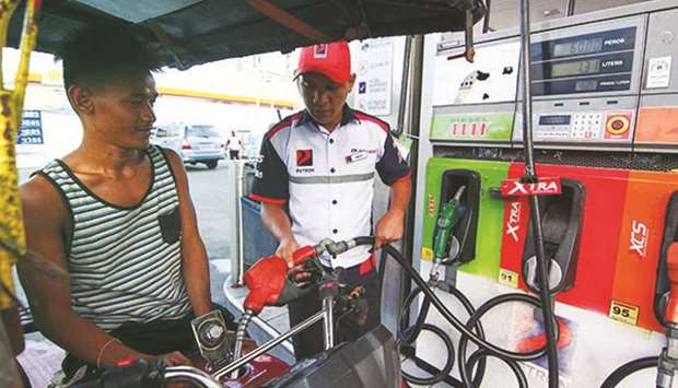 A tricycle driver watches as a gasoline station attendant pumps fuel in a gasoline station at UN Avenue in Manila.