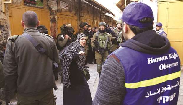 A Palestinian woman stands between Israeli soldiers and Palestinian Youth Against Settlements organisation volunteers (in blue) as Jewish settlers (unseen) tour the Palestinian side of the old city market in Hebron in the occupied West Bank, yesterday.