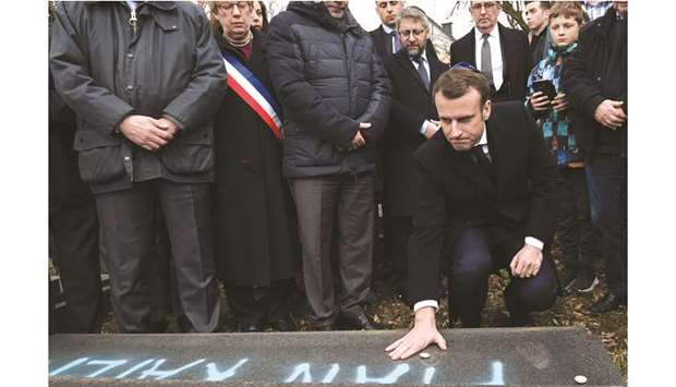Macron places a pebble on a vandalised tomb to pay tribute during his visit at the Jewish cemetery in Quatzenheim, France.