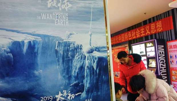 People sitting next to a poster of Chinese sci-fi film ,The Wandering Earth, in Yichang in China's central Hubei province