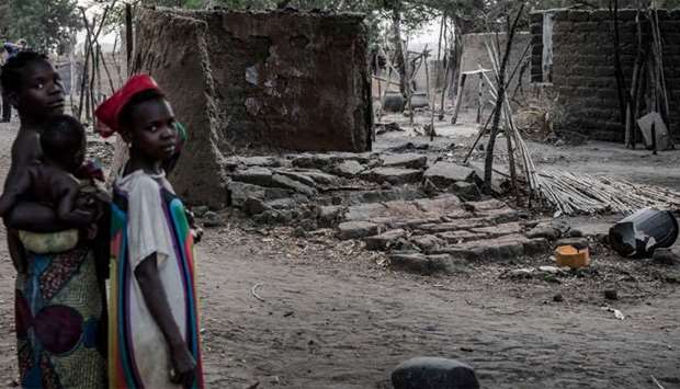 A women and her children stand in front of houses destroyed by a group of herdsmen in Volki, Nigeria