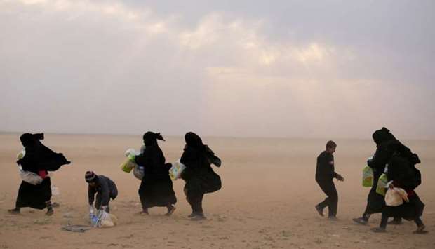 Women walk with their belongings near the village of Baghouz, Deir Al Zor province, Syria