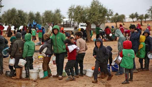 Syrian children queue to receive food distributed by humanitarian aid workers at a makeshift camp for displaced people, near the village of Yazi Bagh