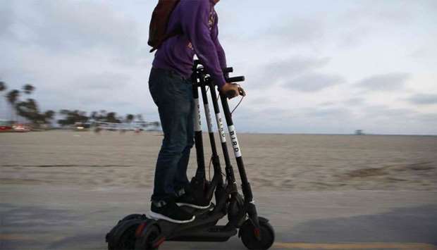 A man rides a Bird shared dockless electric scooter while transporting three others along Venice Beach in Los Angeles