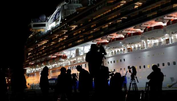 Reporters are silhouetted in front of the cruise ship Diamond Princess are lighted as the vessel is prepared for the transfer passengers tested positive for the novel coronavirus, at Daikoku Pier Cruise Terminal in Yokohama, south of Tokyo