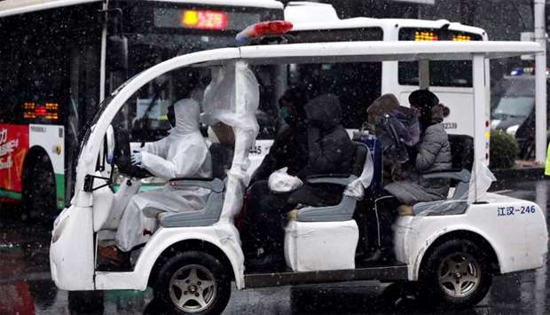 Worker in protective suit drives a vehicle amid snow to transport novel coronavirus patients outside a hospital in Wuhan