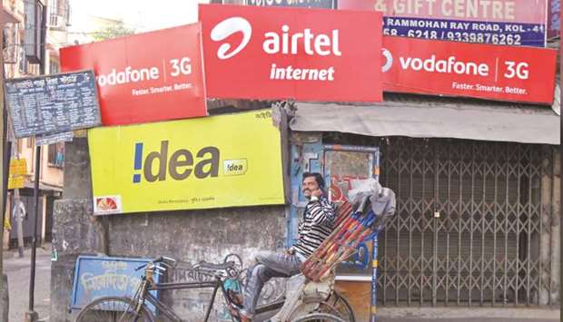 A rickshaw puller speaks on his mobile phone as he waits for customers in front of advertisement billboards belonging to telecom companies in Kolkata (file). Vodafone Ideau2019s woes highlight the struggle Indian telecommunications companies have faced in a market plagued by high spectrum and licence fees, frequent policy flip-flops and endless tax demands.