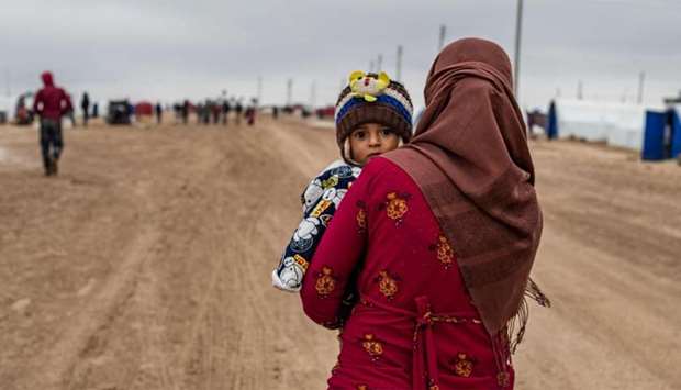 A Syrian woman carrying a child walks by, in the Washukanni Camp for the internally displaced, near the predominantly Kurdish city of Hasakeh in northeastern Syria