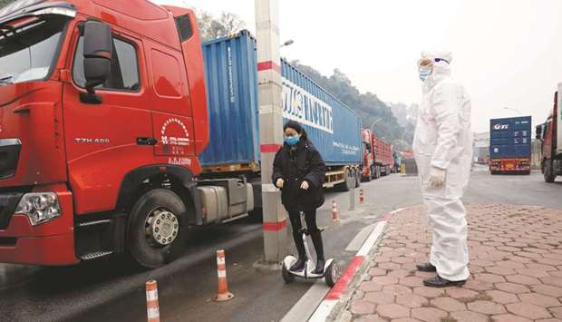 A Vietnamese health worker looks on as a Chinese trader in protective mask rides a hoverboard along container trucks going from China to Vietnam, at Huu Nghi border gate connecting with China, in Lang Son province, Vietnam.