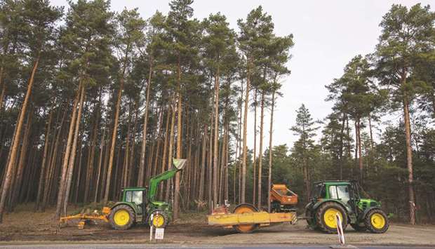 An excavator and a tractor drawn road roller sit beside a forest access road as a truck enters during groundworks for the Tesla Gigafactory in Gruenheide on January 13. A Berlin-Brandenburg court on Thursday ruled that Tesla can resume cutting down trees at a forest site in the small town of Gruenheide to make way for its first assembly plant in Europe.