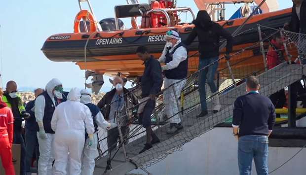 Medical officials wearing protective suits assist a migrant disembarking from 'Open Arms' rescue ship in Pozzallo